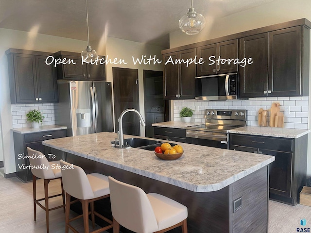 kitchen featuring appliances with stainless steel finishes, decorative light fixtures, an island with sink, decorative backsplash, and sink