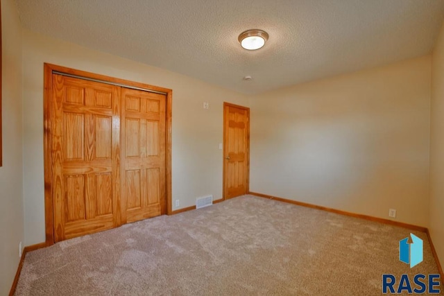 unfurnished bedroom featuring light colored carpet, a textured ceiling, and a closet