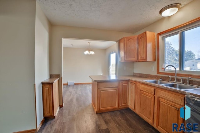 kitchen featuring dark wood-type flooring, sink, kitchen peninsula, dishwasher, and pendant lighting