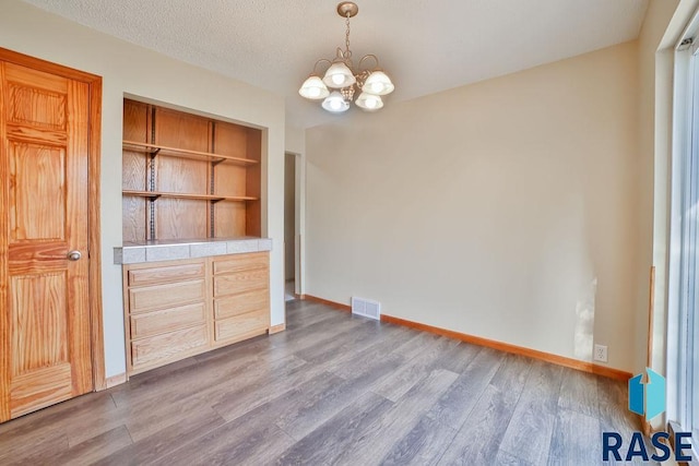 unfurnished dining area featuring a chandelier, light hardwood / wood-style floors, and a textured ceiling