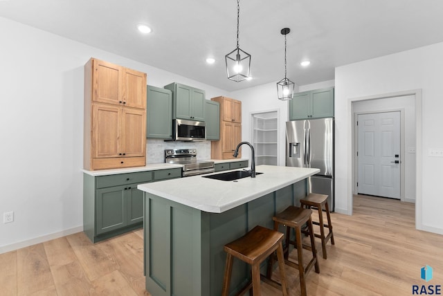 kitchen with a center island with sink, sink, light wood-type flooring, appliances with stainless steel finishes, and decorative light fixtures