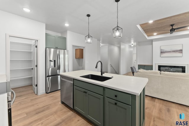 kitchen featuring stainless steel appliances, a kitchen island with sink, sink, green cabinetry, and light hardwood / wood-style floors