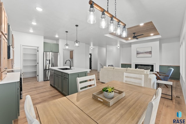 dining room with light hardwood / wood-style floors, a raised ceiling, ceiling fan, and sink