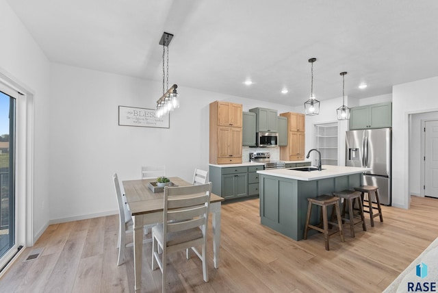 kitchen with appliances with stainless steel finishes, light wood-type flooring, a breakfast bar, sink, and hanging light fixtures