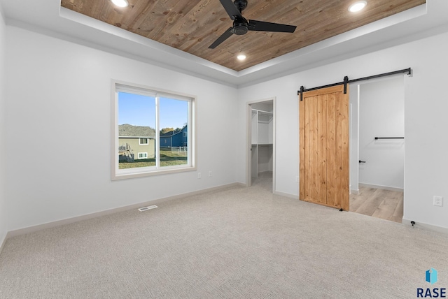 unfurnished bedroom with ceiling fan, a barn door, a tray ceiling, a walk in closet, and wood ceiling