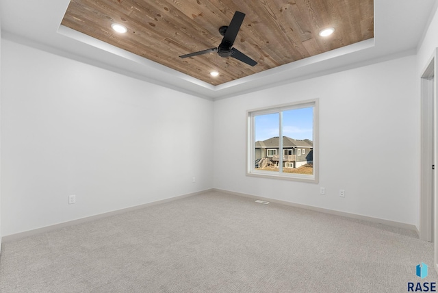 carpeted spare room with a tray ceiling, ceiling fan, and wooden ceiling