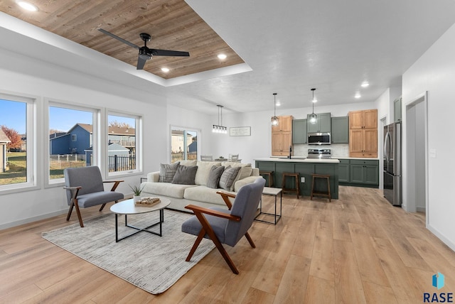 living room featuring a tray ceiling, ceiling fan, light hardwood / wood-style floors, and sink