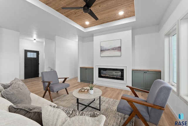 living room with a tray ceiling, ceiling fan, light hardwood / wood-style floors, and wood ceiling