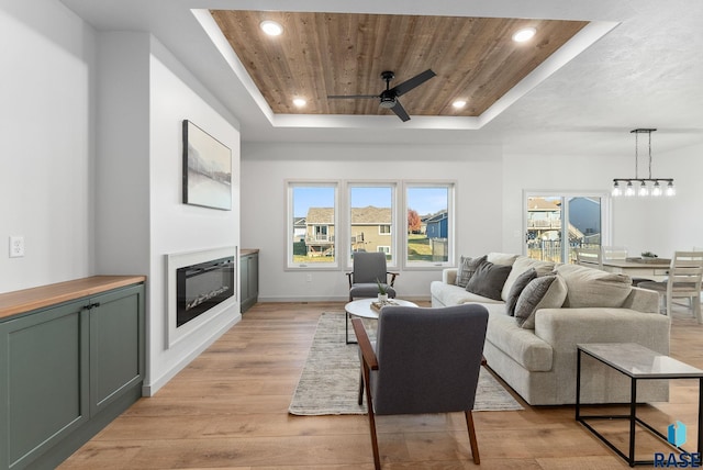 living room with ceiling fan, light hardwood / wood-style floors, wood ceiling, and a tray ceiling