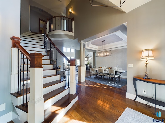 stairs with a towering ceiling, decorative columns, a tray ceiling, hardwood / wood-style floors, and a chandelier