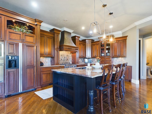 kitchen with a center island with sink, light stone counters, dark hardwood / wood-style flooring, premium range hood, and sink