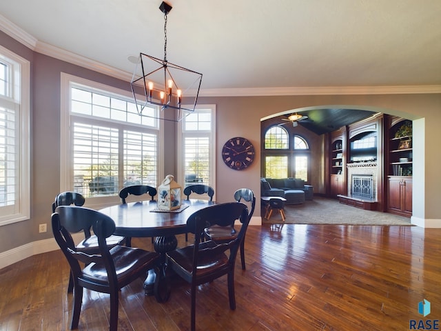 dining area with ceiling fan with notable chandelier, built in features, a tile fireplace, crown molding, and dark hardwood / wood-style floors