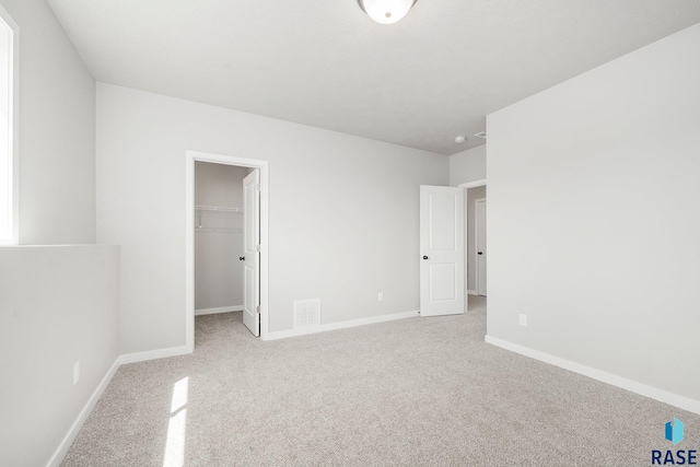 unfurnished bedroom with a walk in closet, a closet, and light colored carpet