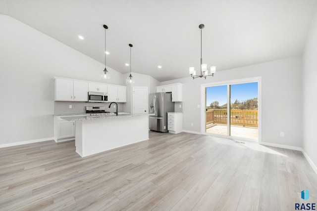 kitchen with lofted ceiling, an island with sink, stainless steel appliances, pendant lighting, and white cabinetry