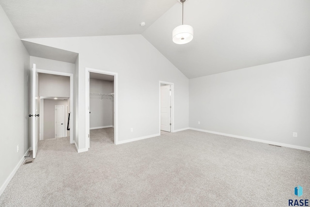 unfurnished bedroom with a spacious closet, vaulted ceiling, light carpet, and a closet