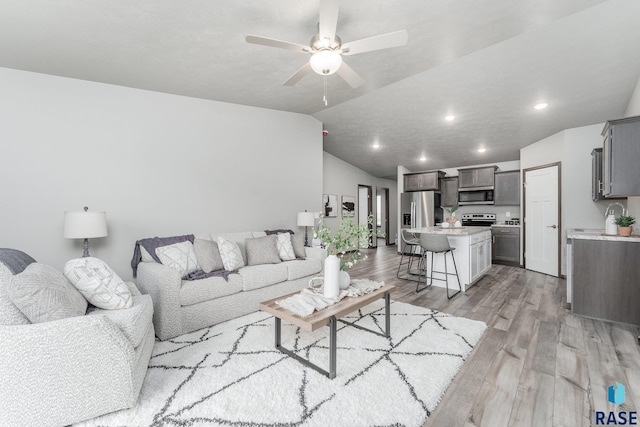 living room with light hardwood / wood-style flooring, vaulted ceiling, and ceiling fan