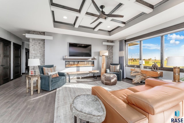 living room featuring a stone fireplace, ceiling fan, coffered ceiling, beamed ceiling, and hardwood / wood-style flooring