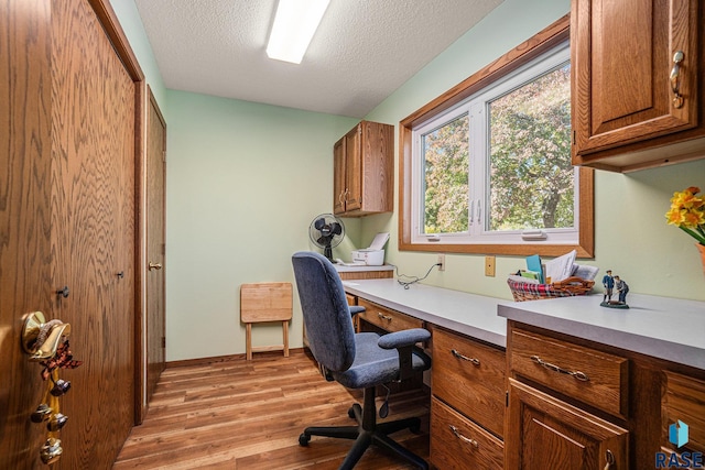 office area with built in desk, a textured ceiling, and light hardwood / wood-style floors