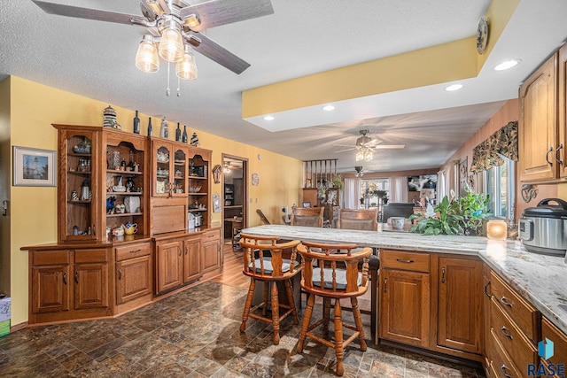 kitchen with light stone countertops, kitchen peninsula, a textured ceiling, and ceiling fan