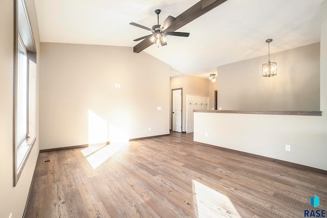 unfurnished living room featuring light hardwood / wood-style flooring, ceiling fan with notable chandelier, lofted ceiling with beams, and plenty of natural light