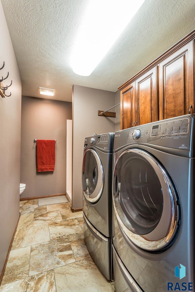 laundry area with washer and clothes dryer, a textured ceiling, and cabinets