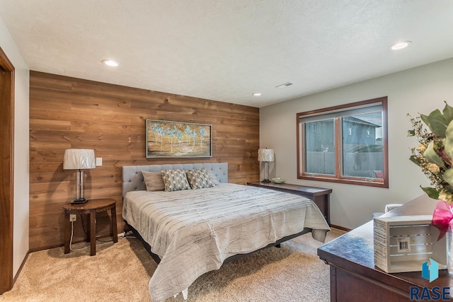 bedroom featuring light carpet, wood walls, and a textured ceiling