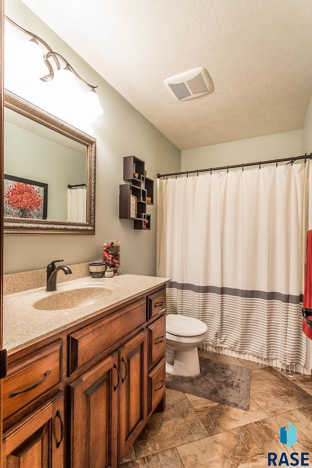 bathroom with vanity, a textured ceiling, walk in shower, and toilet