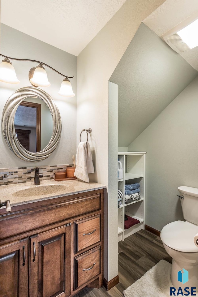 bathroom with vanity, toilet, wood-type flooring, and vaulted ceiling