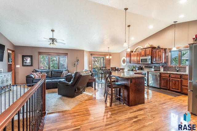 kitchen with light wood-type flooring, ceiling fan with notable chandelier, backsplash, a kitchen breakfast bar, and stainless steel appliances