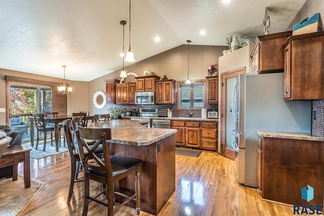 kitchen with lofted ceiling, appliances with stainless steel finishes, pendant lighting, and light wood-type flooring