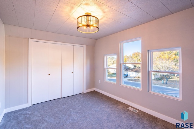 unfurnished bedroom featuring dark carpet, an inviting chandelier, and a closet