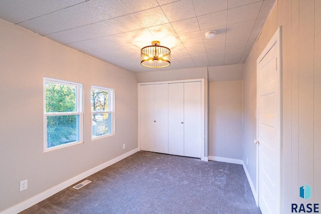 unfurnished bedroom featuring a closet, a notable chandelier, and dark colored carpet