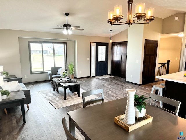 living room featuring ceiling fan with notable chandelier, dark hardwood / wood-style floors, and vaulted ceiling