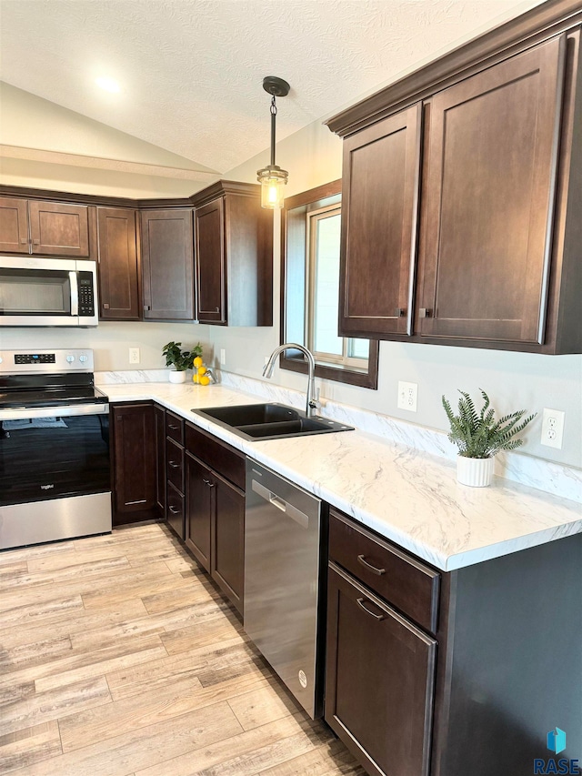 kitchen featuring sink, hanging light fixtures, vaulted ceiling, light wood-type flooring, and appliances with stainless steel finishes