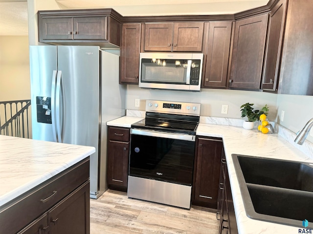 kitchen with dark brown cabinetry, light stone countertops, sink, stainless steel appliances, and light wood-type flooring