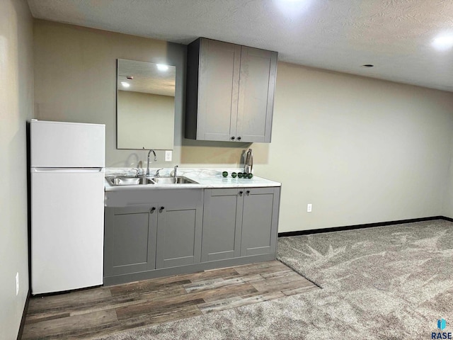 kitchen with a textured ceiling, white fridge, gray cabinetry, and sink