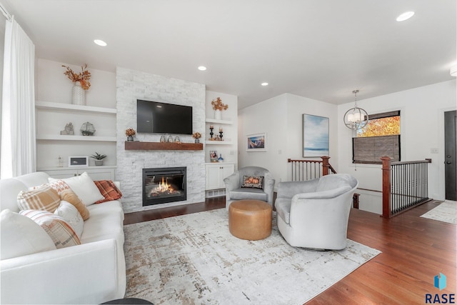 living room featuring built in shelves, a stone fireplace, dark hardwood / wood-style floors, and an inviting chandelier