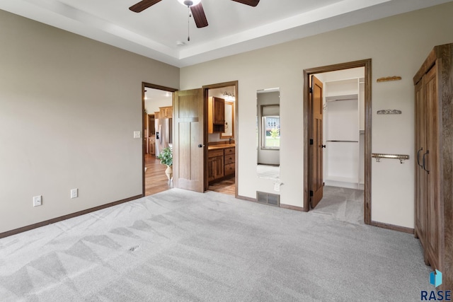 unfurnished bedroom featuring a tray ceiling, a walk in closet, light colored carpet, and ensuite bath