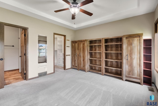 unfurnished bedroom featuring ensuite bath, light carpet, ceiling fan, and a tray ceiling