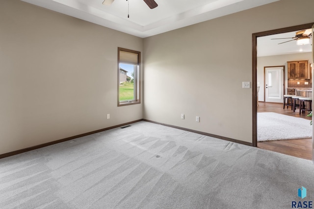 carpeted spare room featuring ceiling fan and a raised ceiling