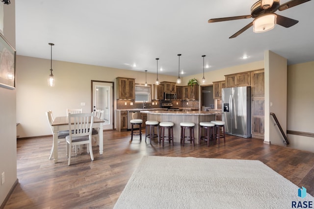 kitchen with tasteful backsplash, hanging light fixtures, appliances with stainless steel finishes, a kitchen breakfast bar, and a kitchen island