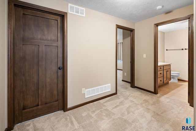 unfurnished bedroom featuring connected bathroom, light carpet, and a textured ceiling