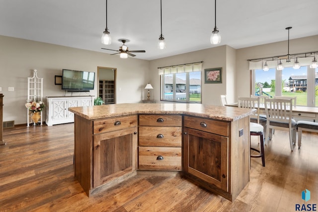 kitchen featuring ceiling fan, hanging light fixtures, light stone counters, a kitchen island, and dark hardwood / wood-style flooring