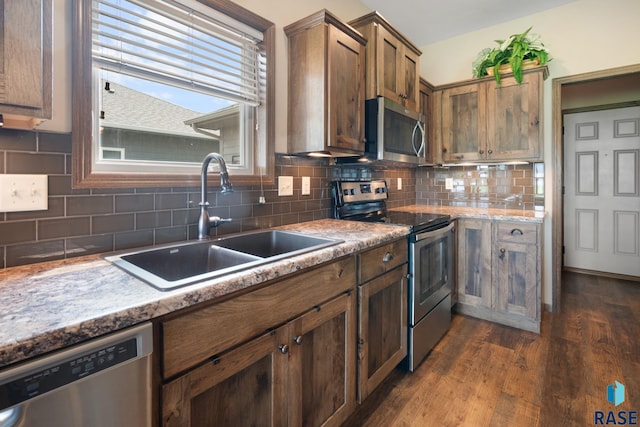 kitchen with sink, appliances with stainless steel finishes, dark hardwood / wood-style floors, light stone counters, and tasteful backsplash