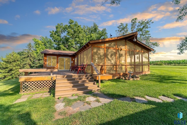 back house at dusk with a wooden deck, a lawn, and a sunroom