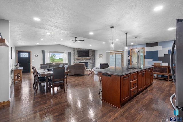 kitchen with hanging light fixtures, a textured ceiling, a kitchen island with sink, vaulted ceiling, and dark wood-type flooring