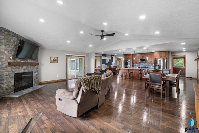 living room with a fireplace, a textured ceiling, ceiling fan, vaulted ceiling, and dark hardwood / wood-style floors