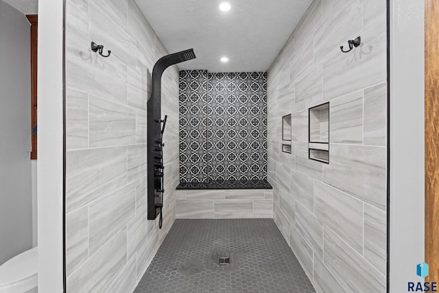 bathroom with tiled shower, a textured ceiling, toilet, and tile patterned flooring