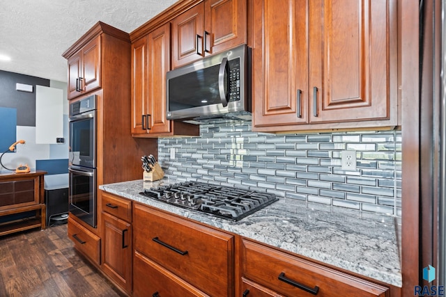 kitchen featuring dark hardwood / wood-style floors, backsplash, light stone countertops, appliances with stainless steel finishes, and a textured ceiling