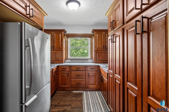 kitchen featuring light stone countertops, a textured ceiling, dark hardwood / wood-style floors, and stainless steel fridge